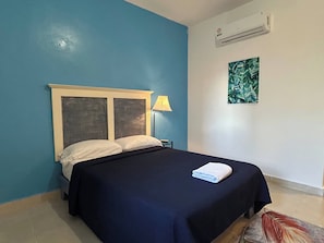 Un lit simple avec une couvre-lit bleu foncé, deux oreillers, une lampe et un appareil de climatisation fixé au mur.