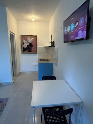 A small room with a white table, a black chair, a television mounted on the wall, and a framed picture on the wall. - Blue Night Aparta Hotel Your haven of peace (Punta Cana)