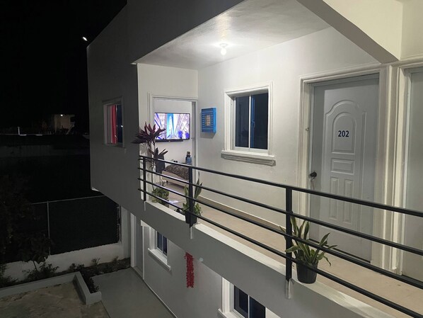 Un edificio de dos pisos con un balcón, un televisor en el nivel superior y una puerta con el número 202.