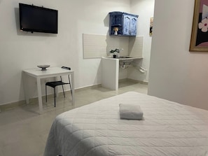 Habitació d'hotel amb un llit, una taula de treball, una cadira, un televisor, un rentanet i un armari.