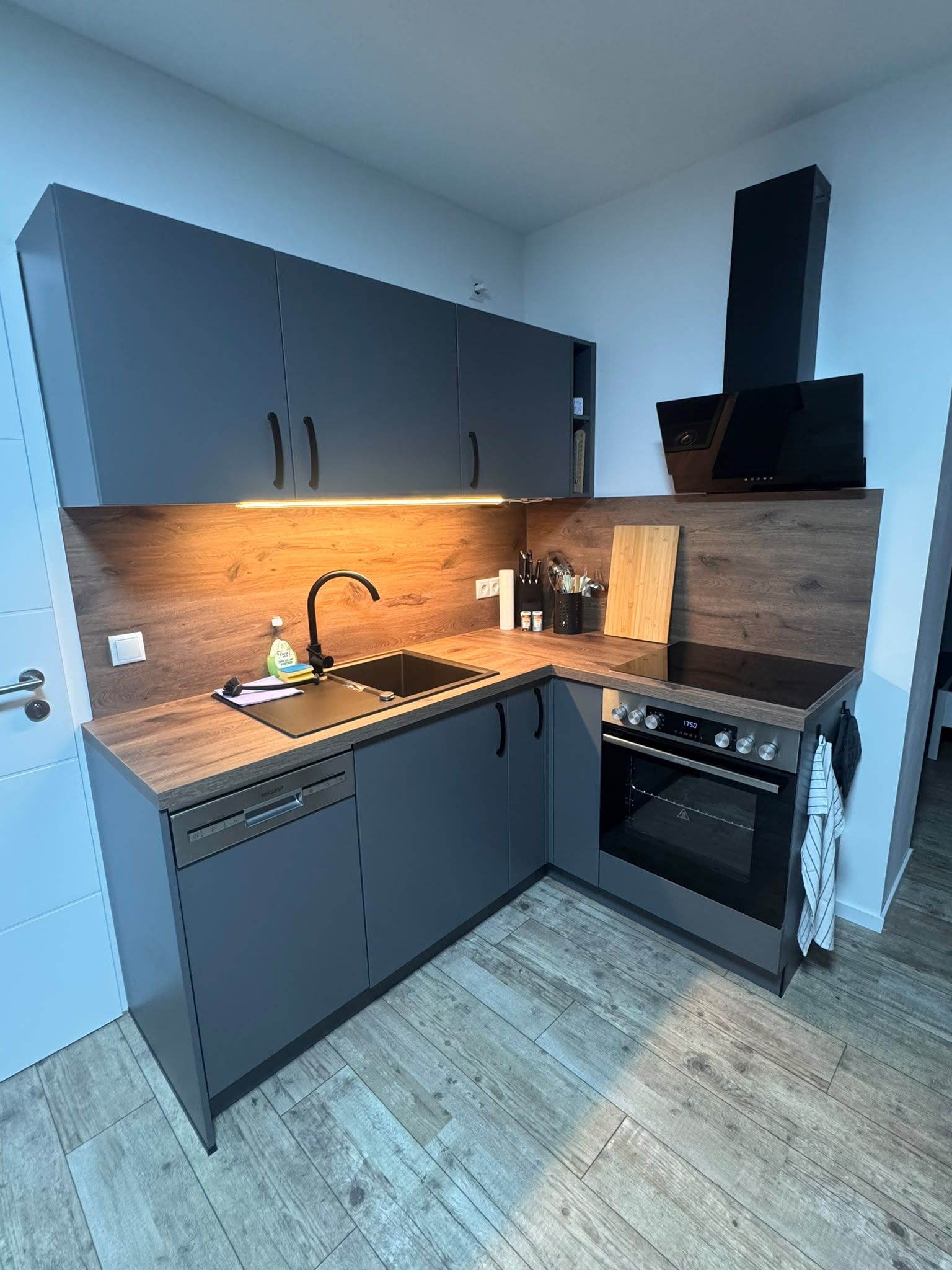 A modern kitchen with grey cabinets, a wooden countertop, a built-in oven, and a dishwasher.