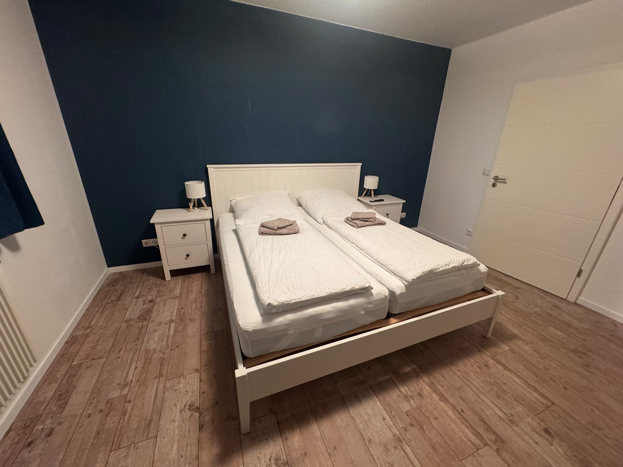 A double bed with a wooden frame, two bedside tables with lamps, and a door to the right.