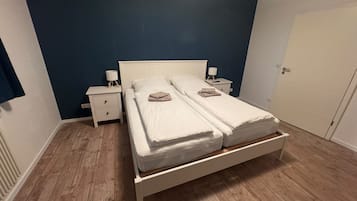 A double bed with a wooden frame, two bedside tables with lamps, and a door to the right.