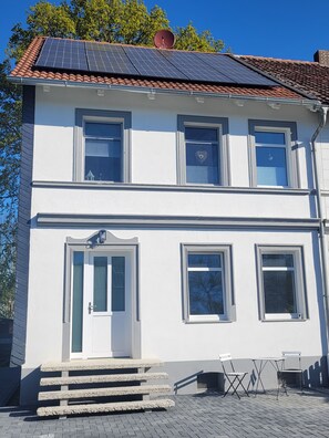 A two-story building with a white facade, a tiled roof, and a small outdoor seating area with a table and chairs. - New Listing (Huy)