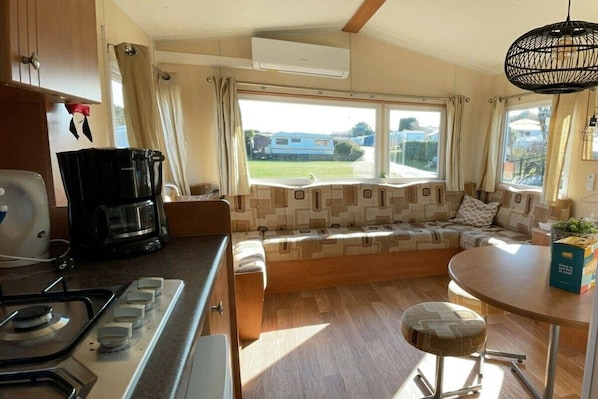 A compact kitchen with a gas stove, a coffee maker, and a window seat with cushions.