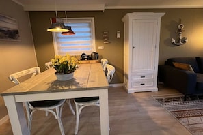 A dining area with a wooden table and chairs, a potted plant, and a window with blinds.