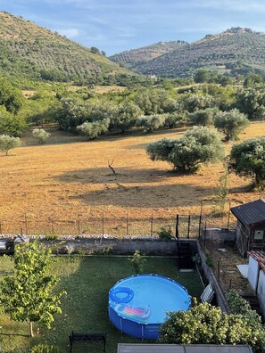 Ein Garten mit einem blauen aufblasbaren Pool, einem eingezäunten Bereich und Blick auf eine hügelige Landschaft.
