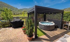 A covered outdoor area with a hot tub, a grill, and potted plants.