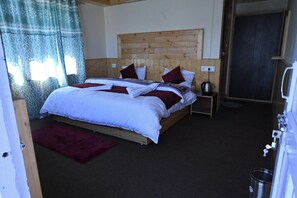 A room with a wooden headboard bed, a red throw blanket, a small bedside table with a kettle, and a dark carpet. - Snow Lotus Kalpa (Jangal Mehfuza Mehduda C-)