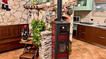 A kitchen with a stone wall, a wood-burning stove, a wooden cart, and a Christmas tree.