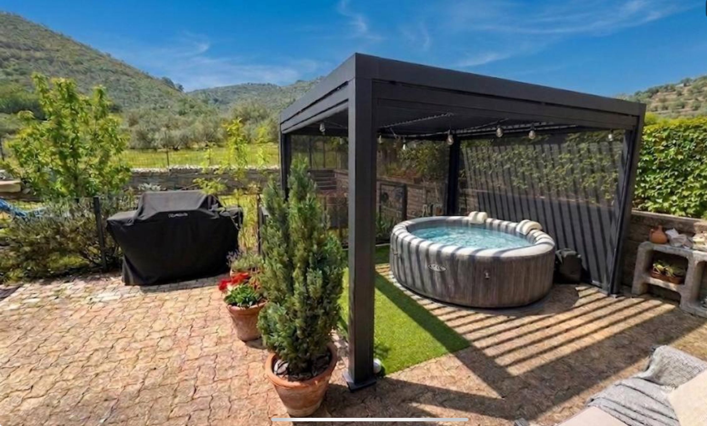 Un espacio al aire libre techado con un jacuzzi, una parrilla y plantas en macetas.