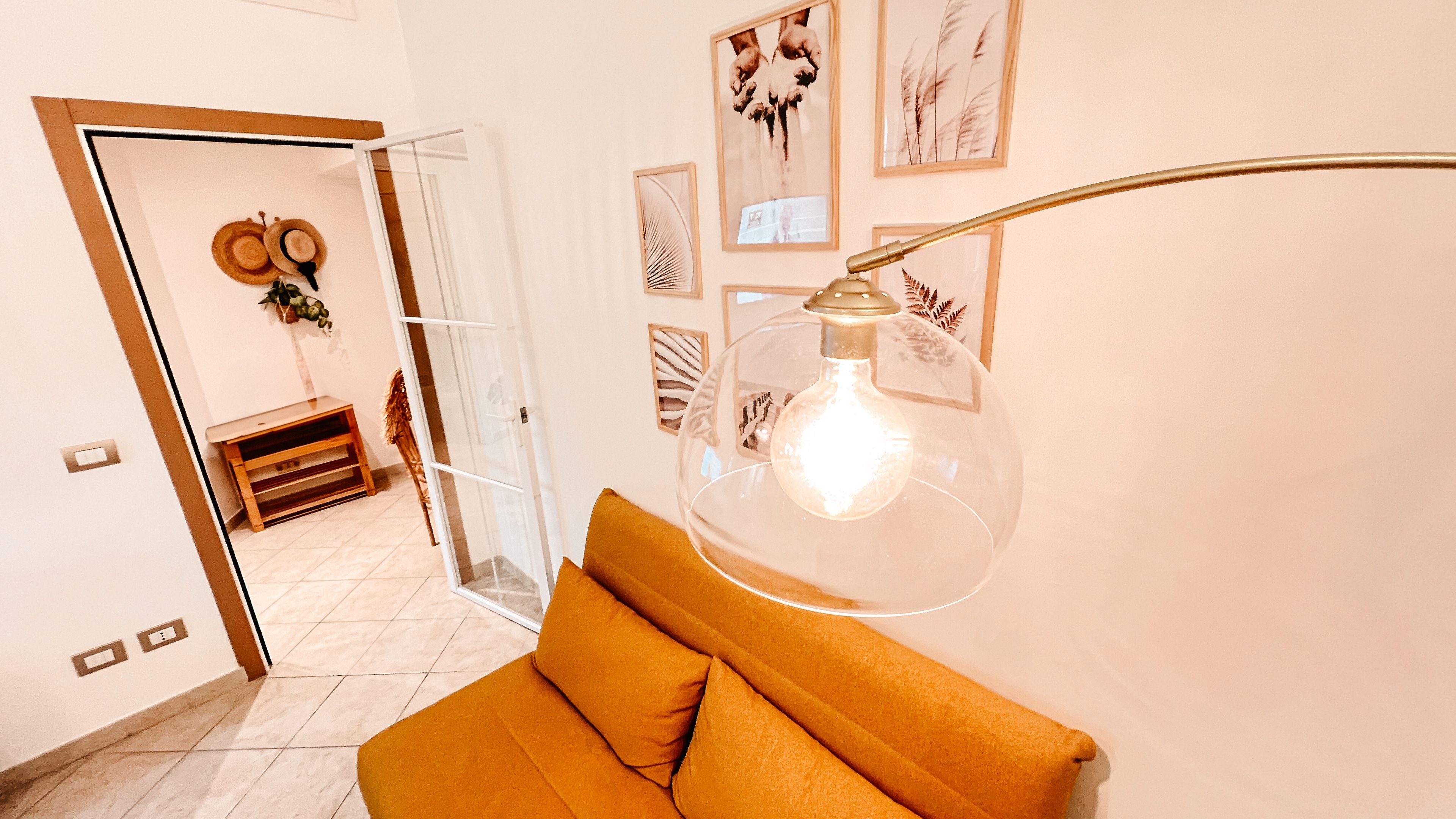 A room with a clear glass door leading to a hallway, a round table with chairs, and a wall-mounted light fixture.