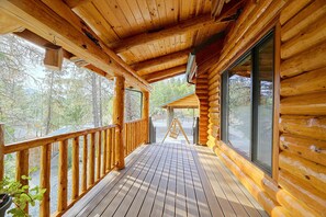 A wooden deck with a railing, large windows, and a view of the surrounding forest.