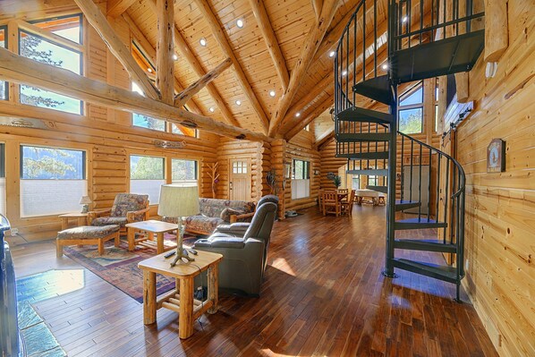 A log cabin interior with a wooden floor, a fireplace, a sofa, and a staircase.