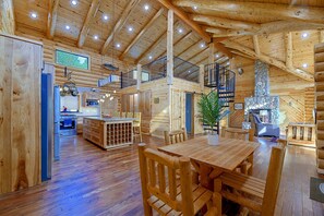 A spacious wooden cabin interior with a dining area, kitchen, and a stone fireplace.
