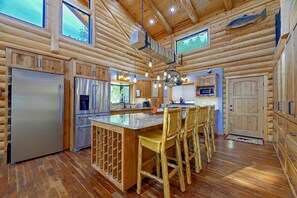 A log cabin-style kitchen with wooden cabinetry, a stainless steel refrigerator, and a central island with bar stools.