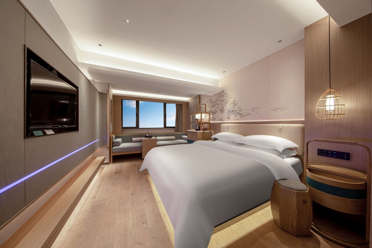 Een moderne hotelkamer met een groot bed, een flatscreen televisie, een bureau en uitzicht op de lucht.
