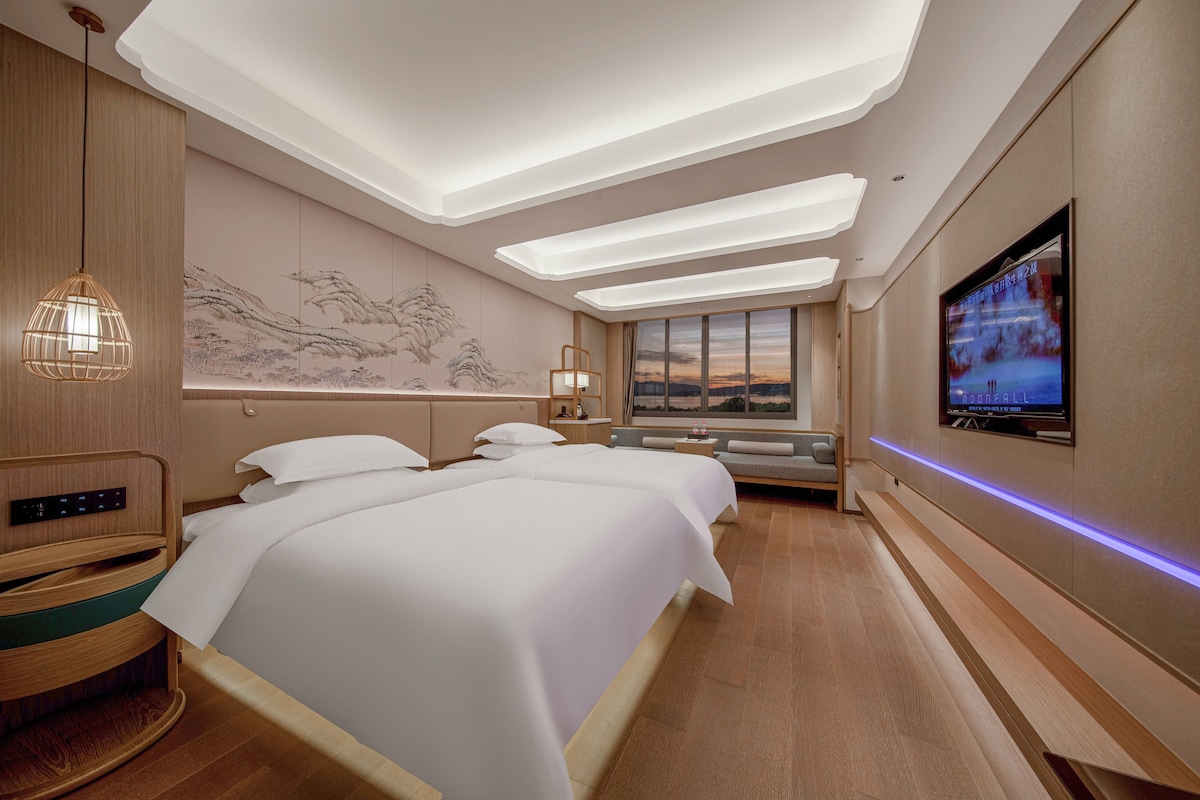 Een hotelkamer met een groot bed, een televisie, een bureau en uitzicht op de zonsondergang.