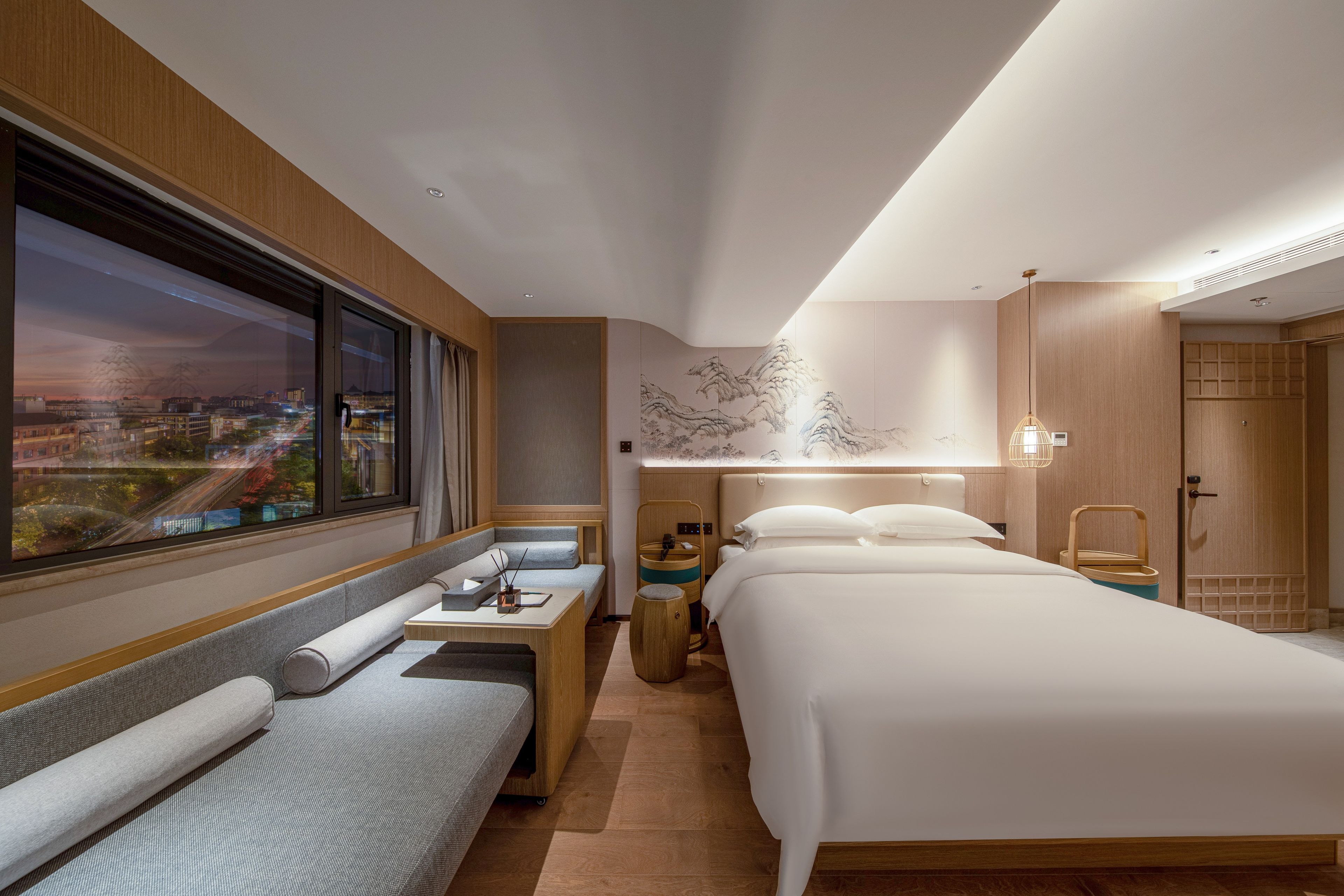 Une chambre d’hôtel comprenant un lit, un coin salon, un bureau et une grande fenêtre donnant sur la ville.