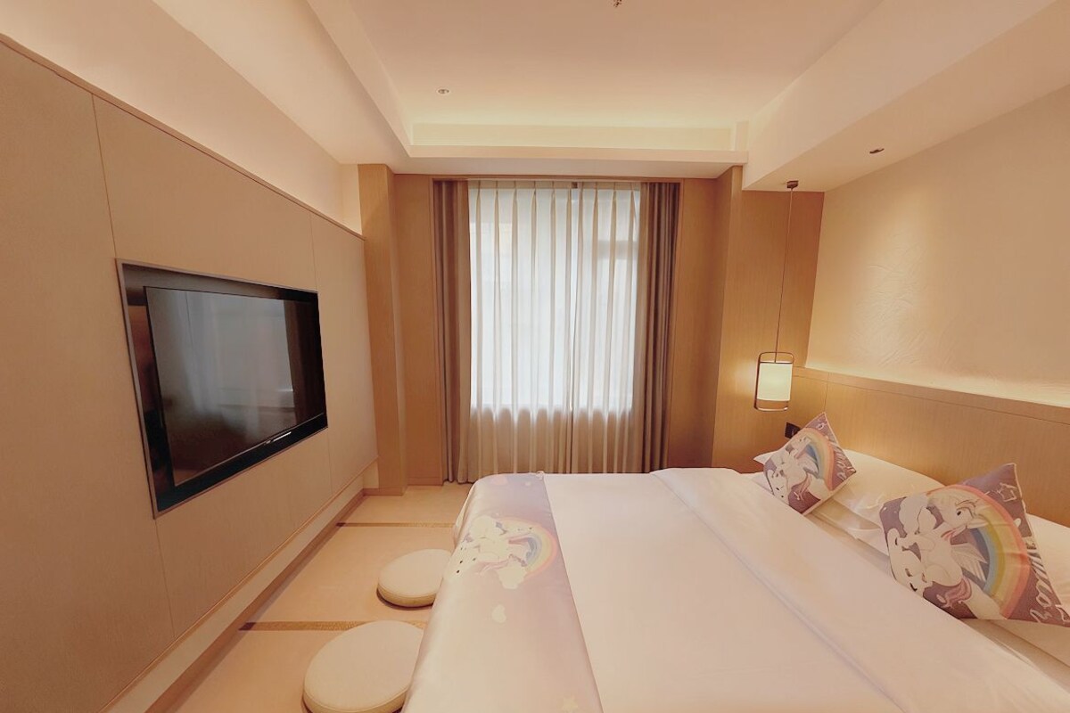 Een hotelkamer met een bed, een televisie, een raam met gordijnen en een bedlamp.