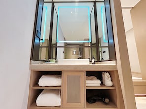 Een badkamer met een grote spiegel, een wastafel en planken met handdoeken.