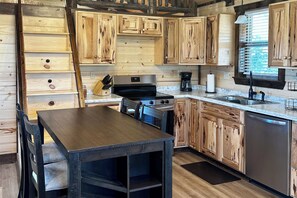 A kitchen with wooden cabinetry, a stove, a sink, and a dining area with a table and chairs. - RimRock Ranch Retreat Near Fort Robinson Trails (Crawford)