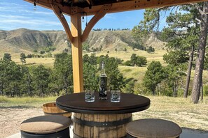 A wooden table with a bottle and glasses, set against a mountainous backdrop. - RimRock Ranch Retreat Near Fort Robinson Trails (Crawford)