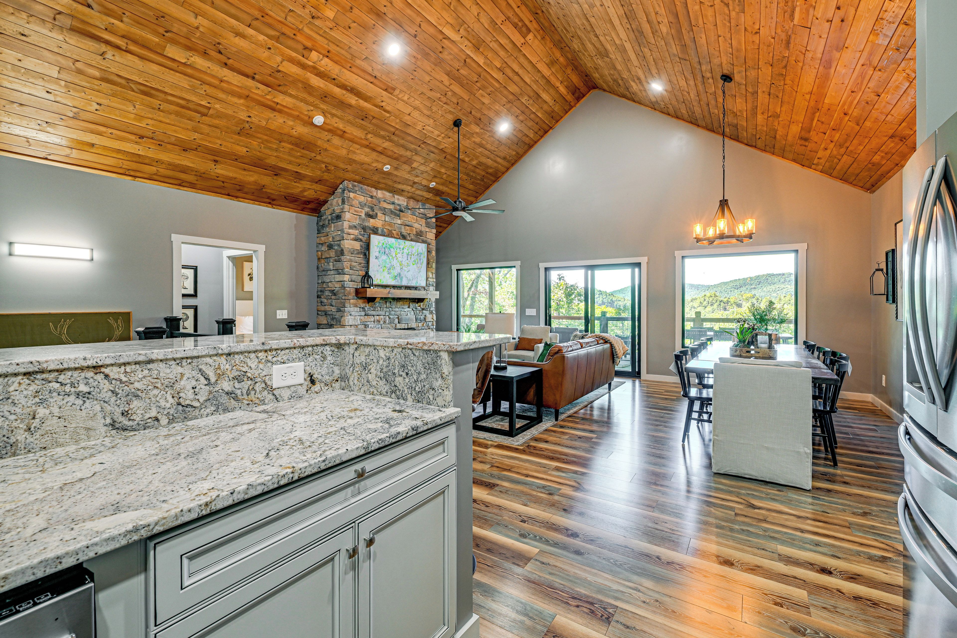 A spacious kitchen with granite countertops, a stone fireplace, and a dining area with a high ceiling and wooden beams.