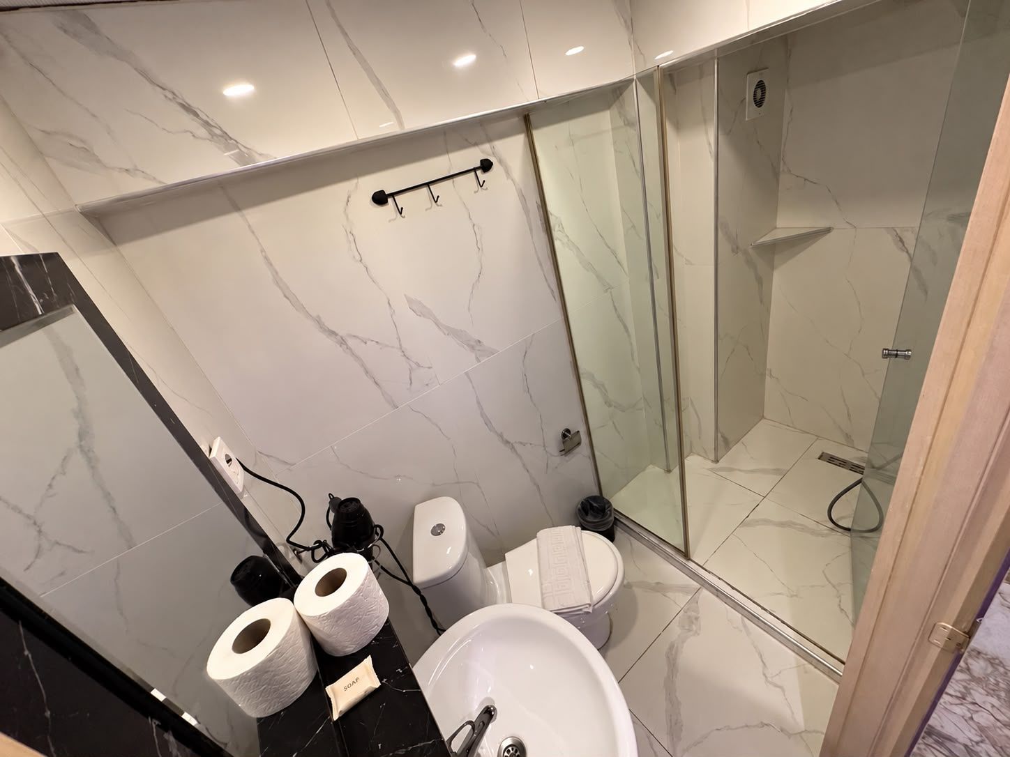 A modern bathroom with a marble floor, a glass-enclosed shower, a sink, and two toilets.