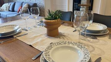 Un tavolo da pranzo apparecchiato con piatti, bicchieri e posate, un vaso con una pianta e un divano sullo sfondo.