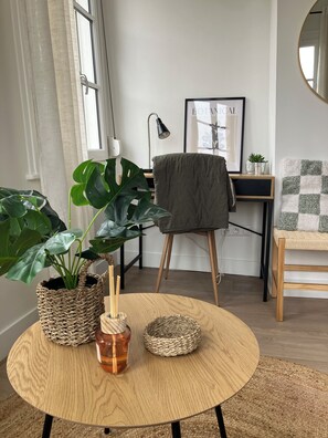 Huoneessa on pyöreä puupöytä, ruukkukasvi, lamppu ja tuoli.