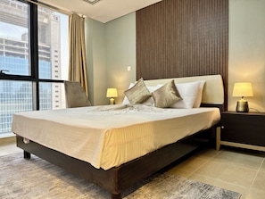 A hotel room with a large bed, two bedside lamps, a view of the city through a window, and a wooden panel wall. - Star by Azizi (Dubai)
