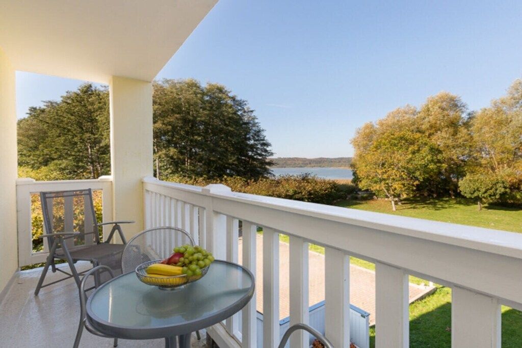 A balcony with a table and chairs, overlooking a body of water and trees.