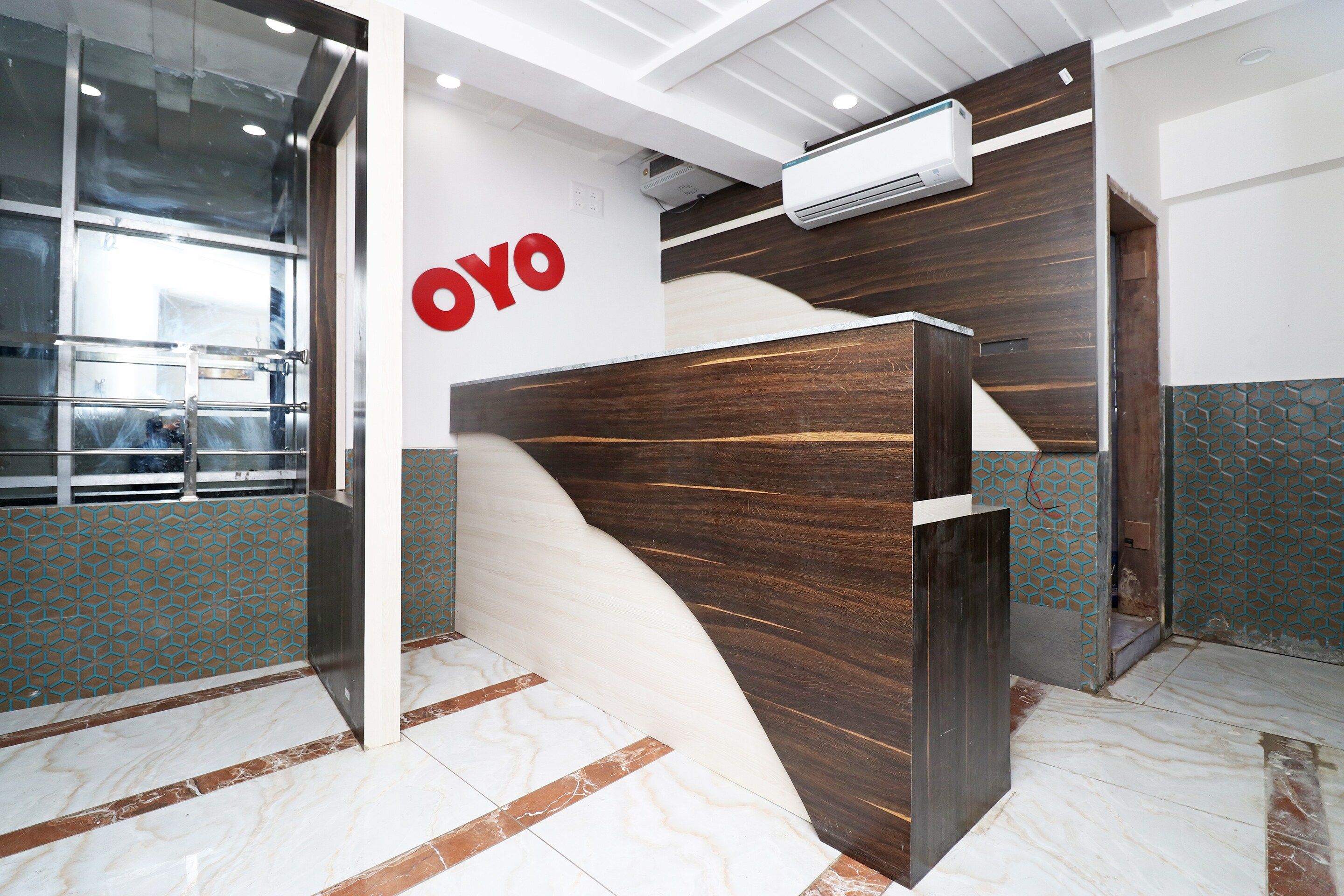 A reception desk with a wooden finish, a wall-mounted air conditioning unit, and a geometric patterned wall.