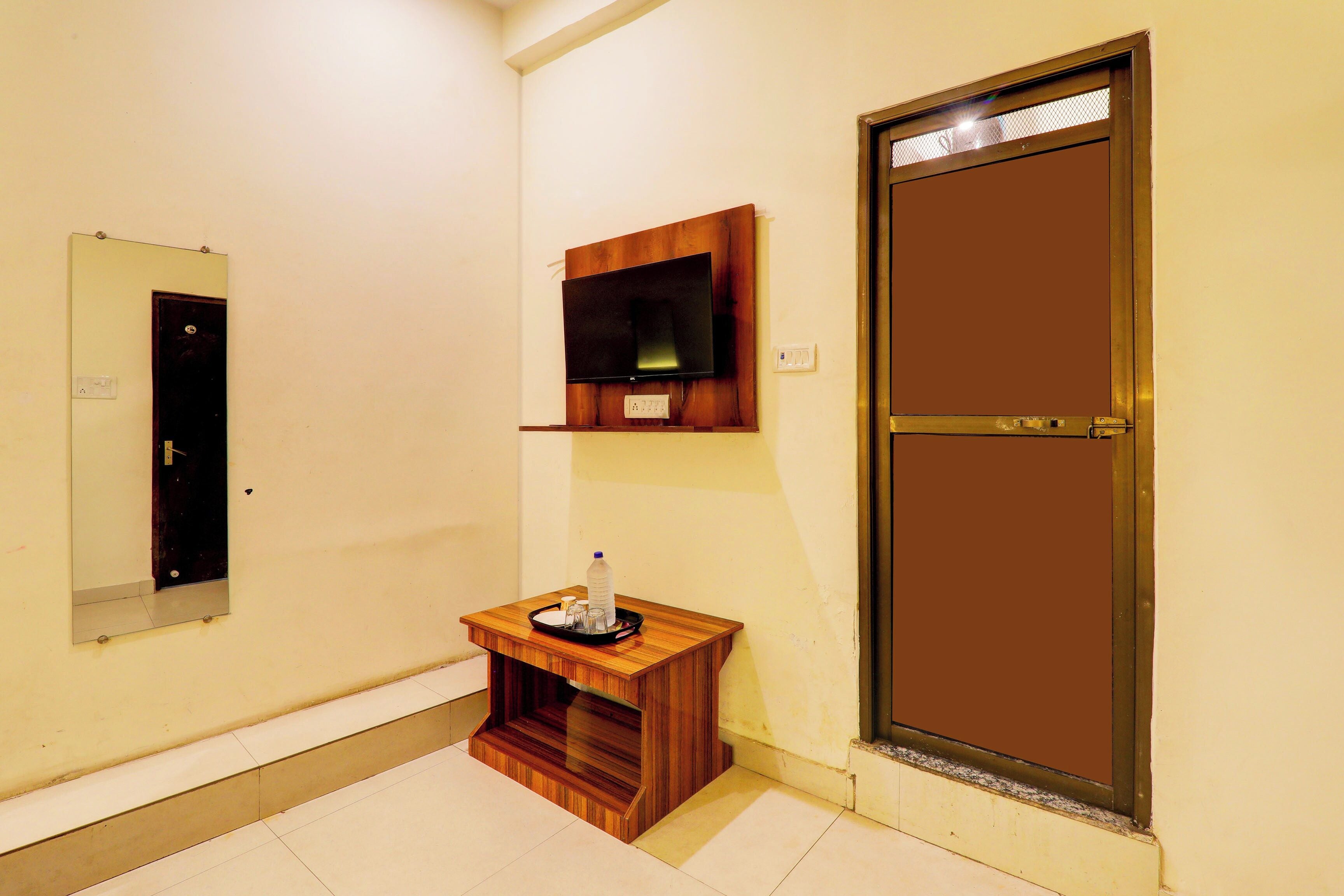 Habitación de hotel con tocador de madera, un espejo, un televisor de pantalla plana montado en la pared y una puerta con manija metálica.