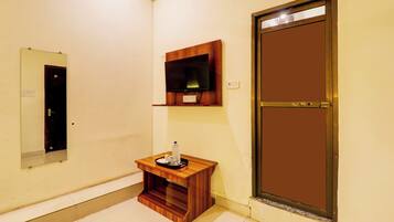 Habitación de hotel con tocador de madera, un espejo, un televisor de pantalla plana montado en la pared y una puerta con manija metálica.