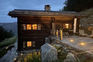A rustic log cabin with a stone porch, multiple windows, and a stone staircase leading to the entrance.