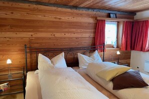 A wooden-paneled room with a bed, two bedside tables, and a window with red curtains.