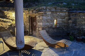 A stone building with a wooden door and a heart-shaped decoration, a wooden bench, and a white umbrella.