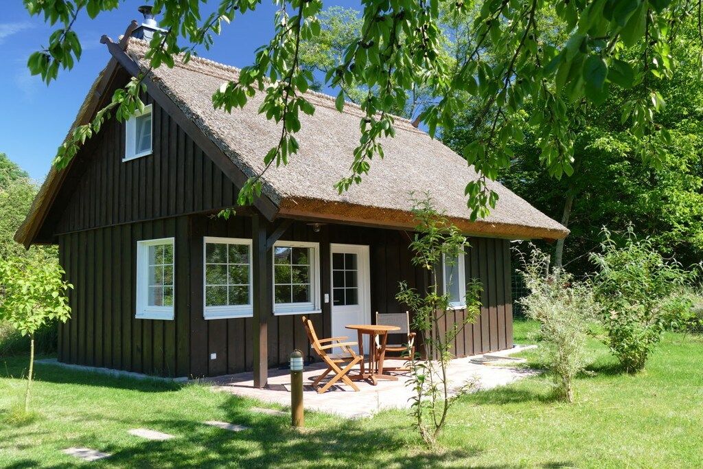A wooden cabin with a thatched roof, a small porch, and a seating area with chairs and a table.