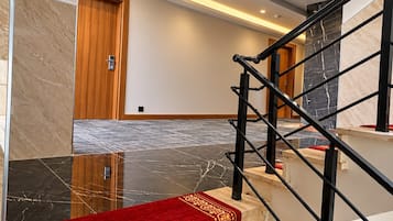 Un interior moderno con una escalera de mármol, una puerta de madera y una zona con alfombra roja.