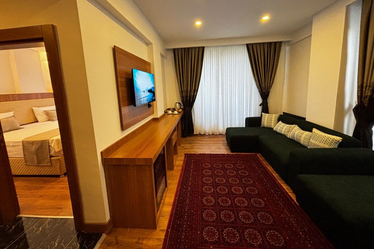 A hotel room with a bed, a TV mounted on the wall, a sofa, a coffee table, and a patterned rug.