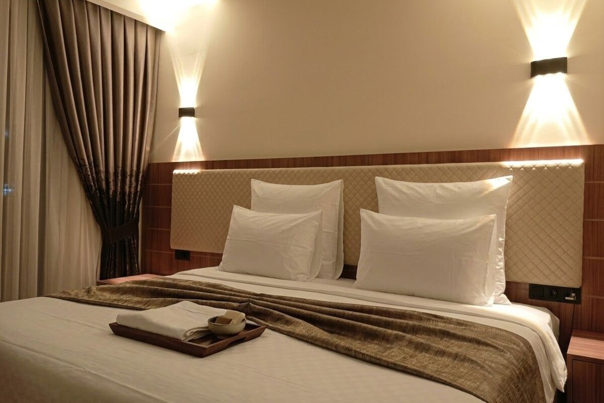 Quarto de hotel com cama, cortinas, luminárias na parede e bandeja com toalhas.