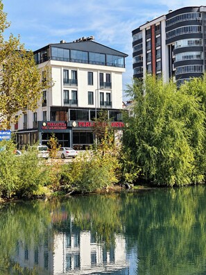 A hotel with a modern facade, a restaurant named 'PERLAVISTA' on the ground floor, and a reflection in the water.