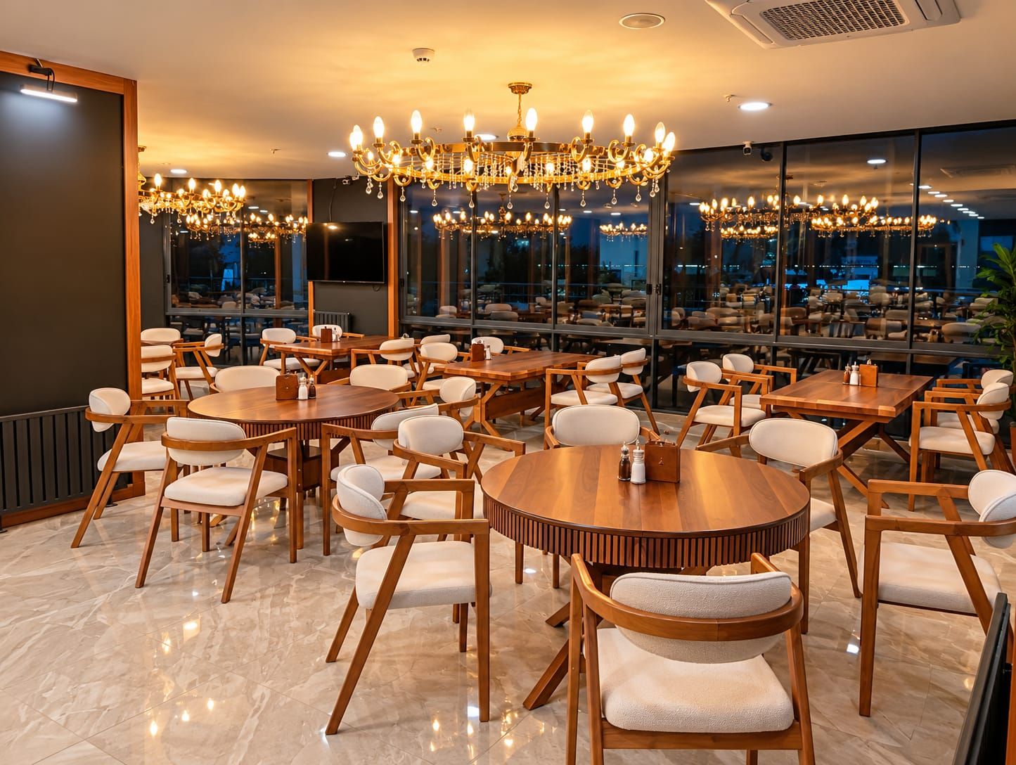 Un ristorante con diversi tavoli e sedie rotondi, ampie finestre e un lampadario.