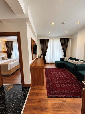 A modern hotel room with a bed, a wooden desk, a green sofa, and a red patterned rug. - Perlavista Otel Cafe Restaurant (Elbistan)