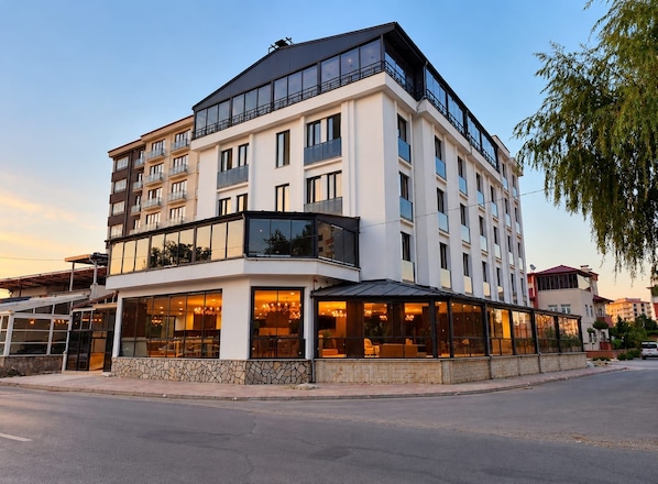 Hotel com vários andares, fachada de vidro, área de estar ao ar livre e base de pedra.