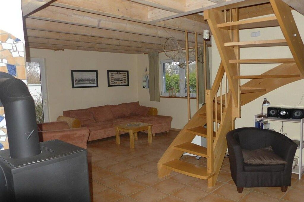 Een woonkamer met een bank, een bijzettafeltje, een open haard, een houten trap en een zwarte fauteuil.