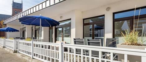 A building with outdoor seating, white railings, and blue umbrellas.