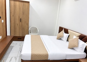 A hotel room with a bed, a wooden wardrobe, and a white chair. - Hotel Shreedha Palace (Indore)